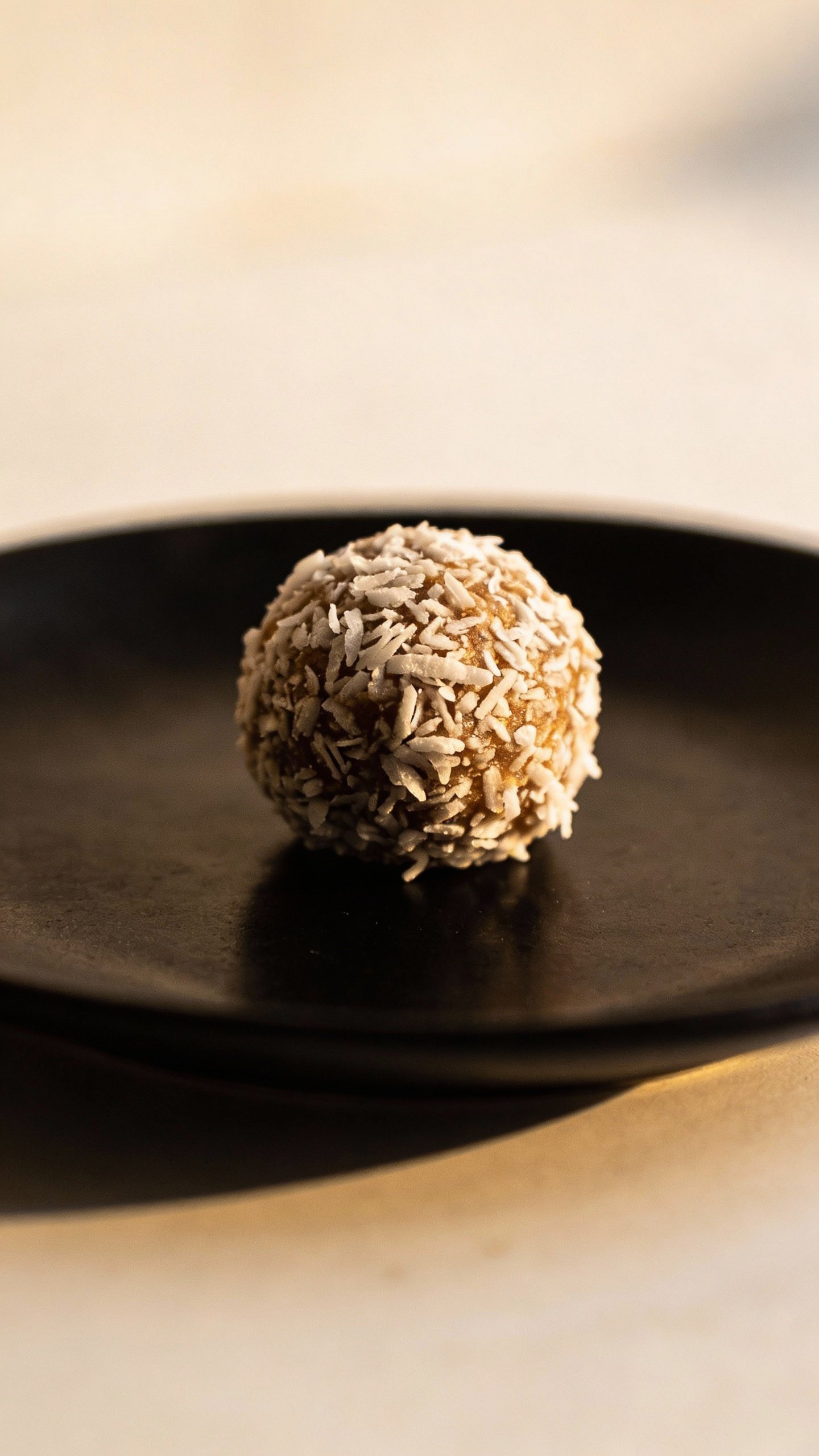 single coconut-coated bliss ball on matte black plate