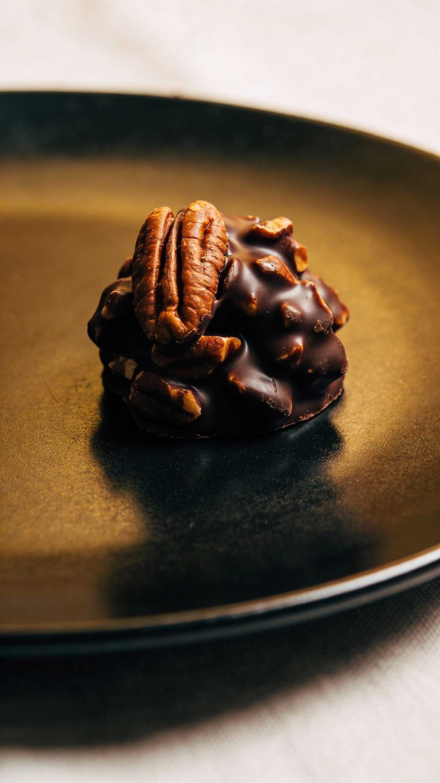 single dark chocolate pecan cluster on matte black plate