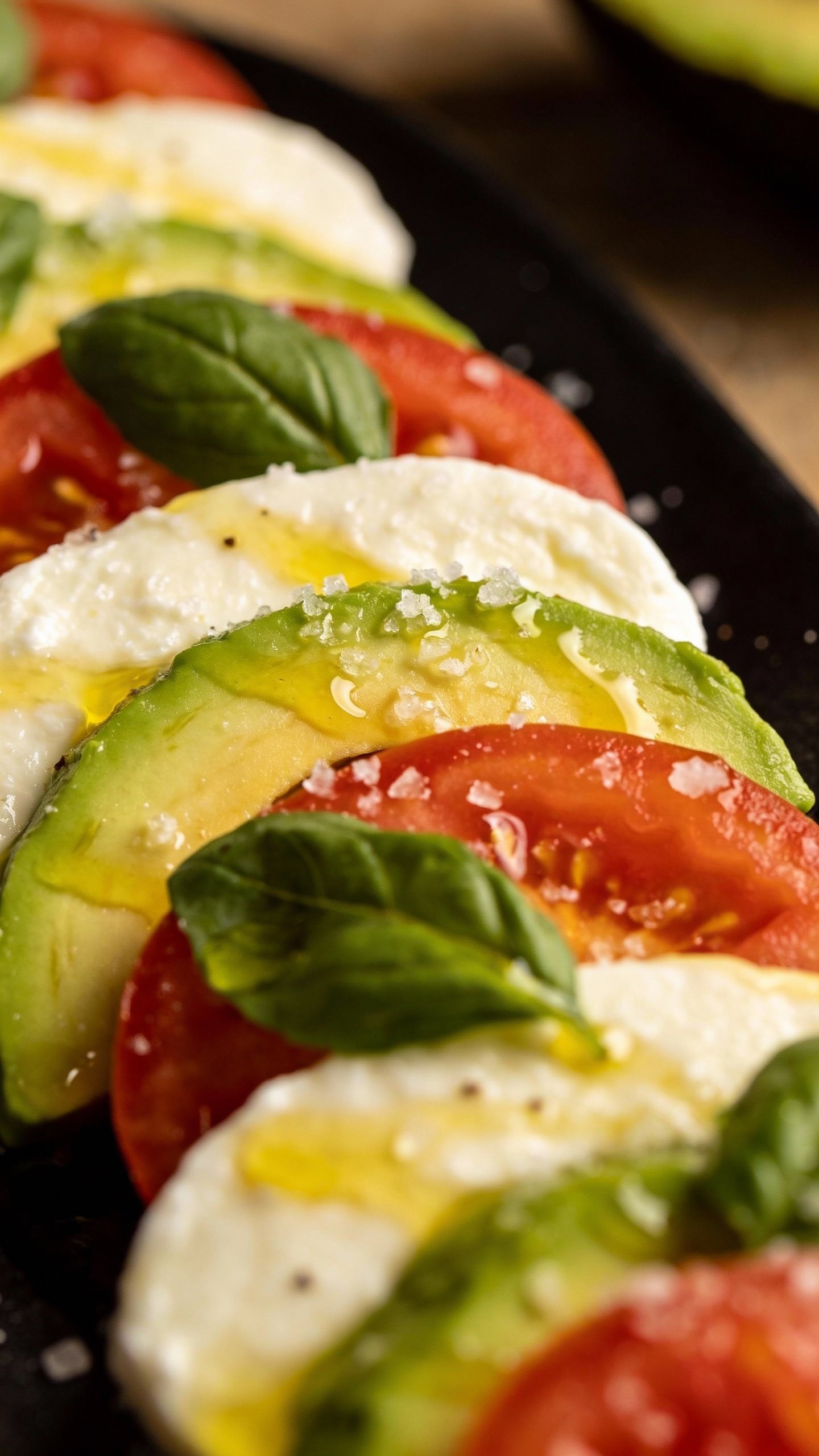 closeup avocado caprese salad on matte black plate
