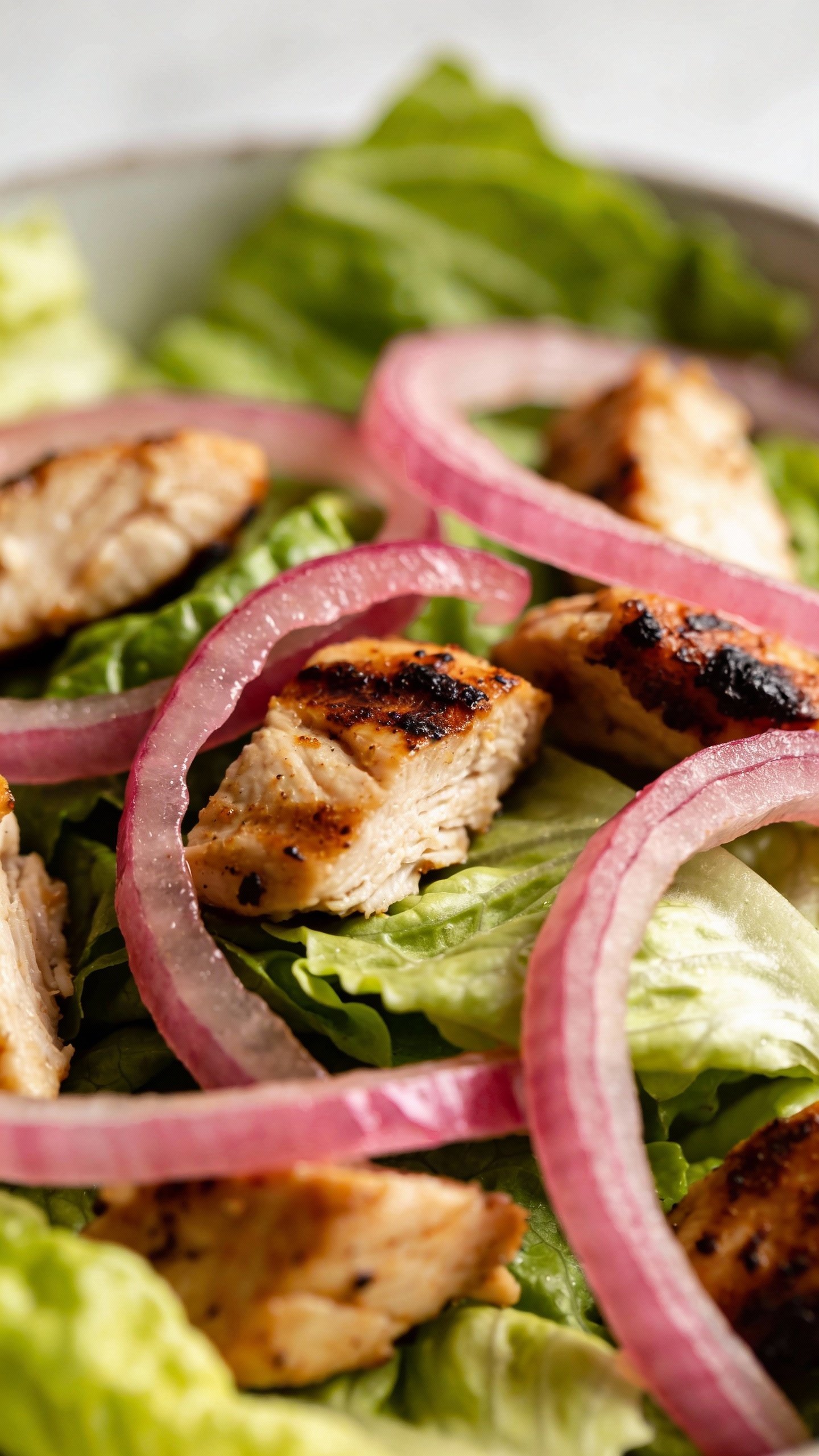 closeup romaine salad topped with smoky chicken and pickled onions