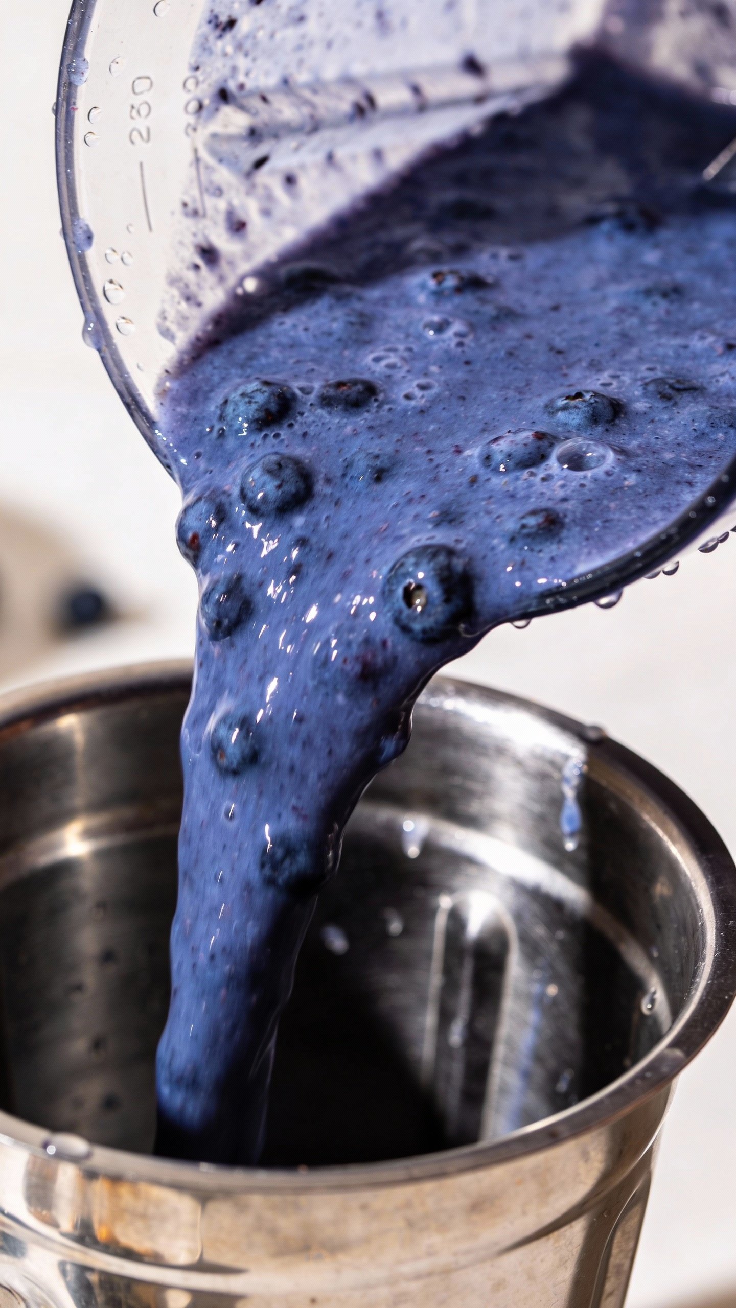 stainless blender jar pouring thick blueberry smoothie stream