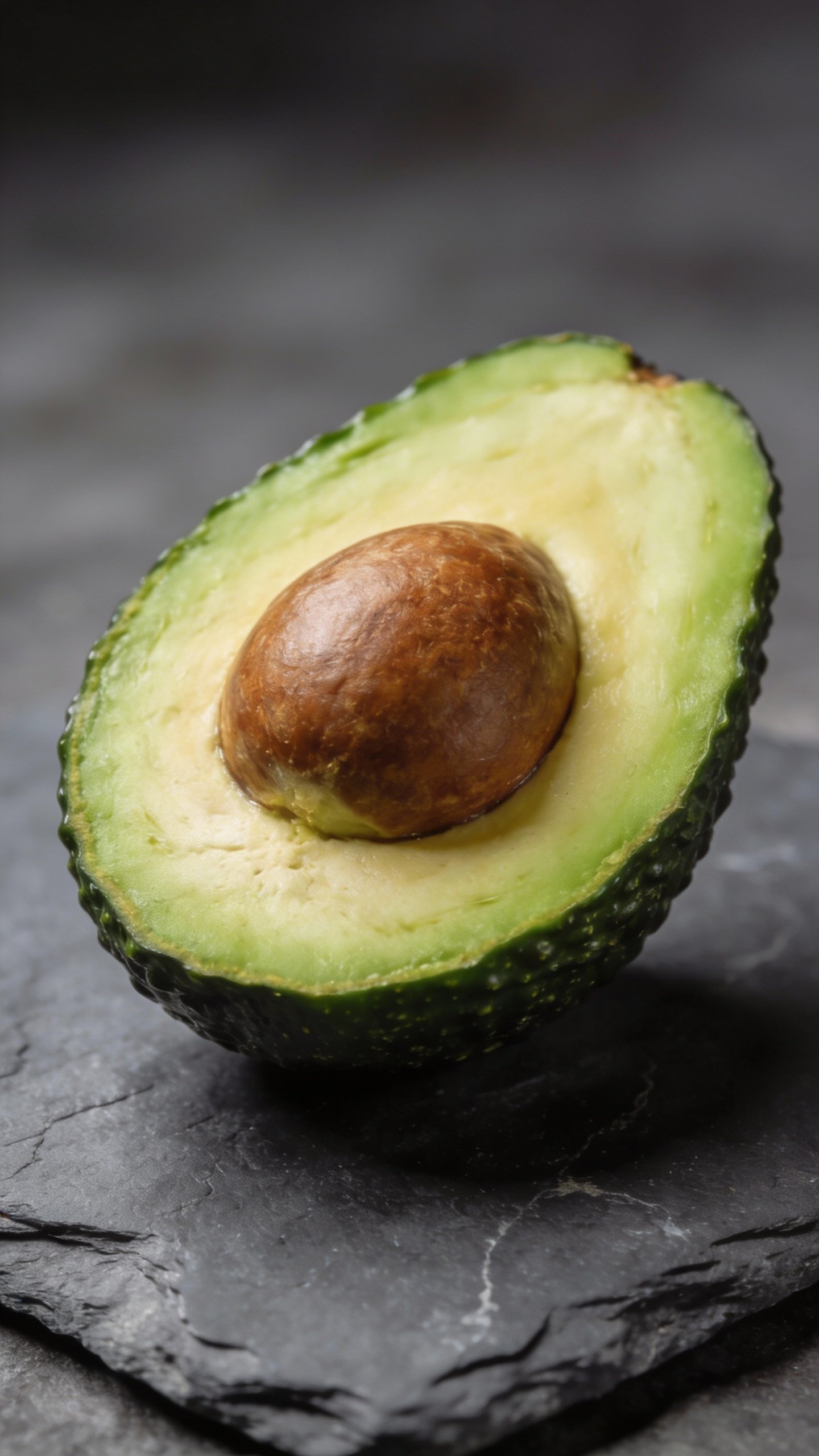 ripe avocado half with seed on slate background, studio lighting