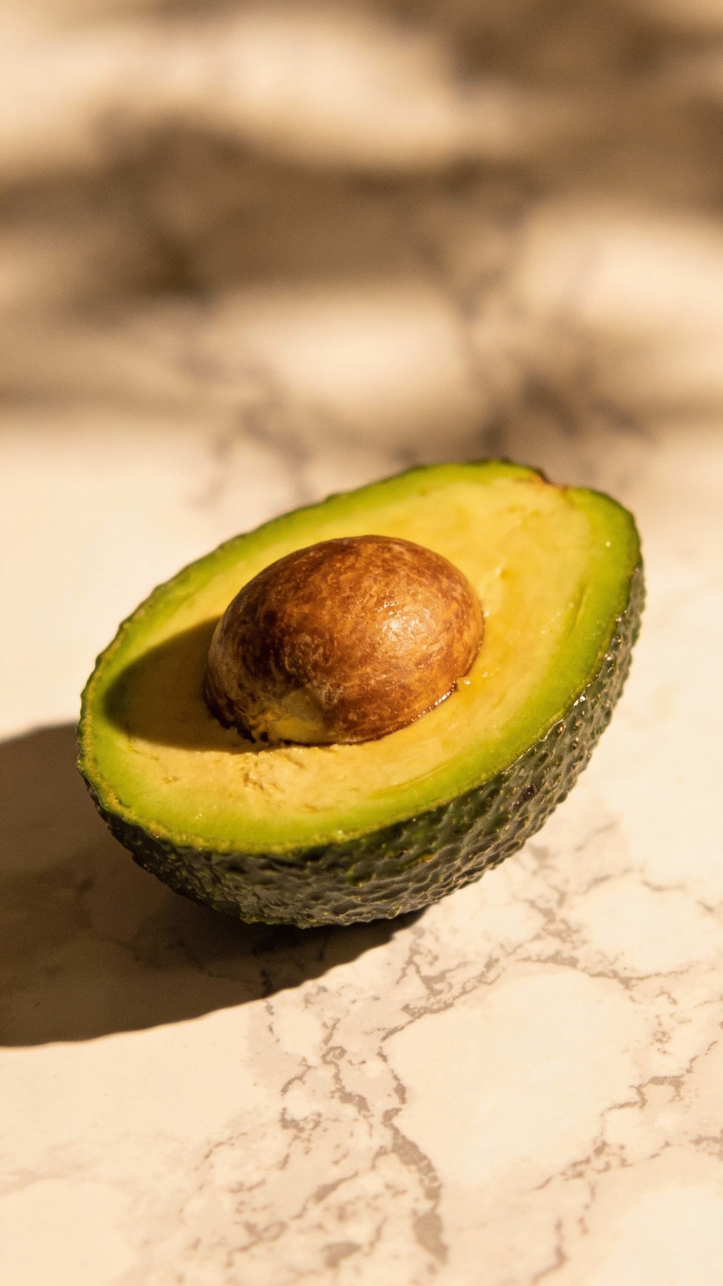 single ripe halved avocado on marble, seed facing up