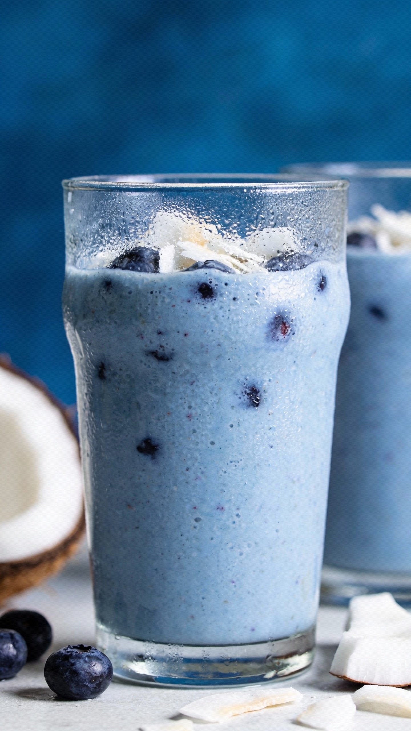 closeup blueberry coconut smoothie in clear glass, frosty condensation