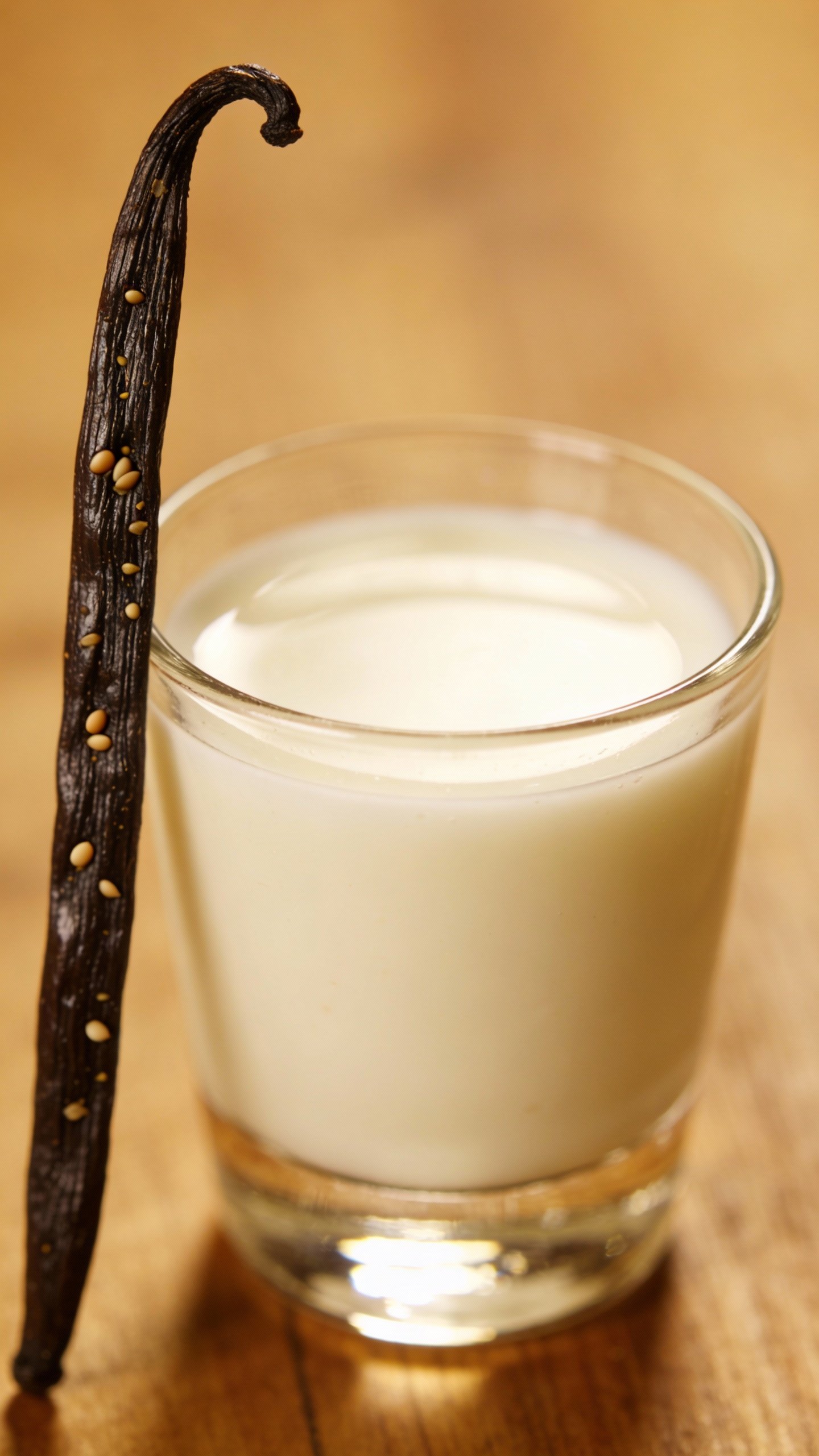 vanilla bean pod next to small glass of almond milk
