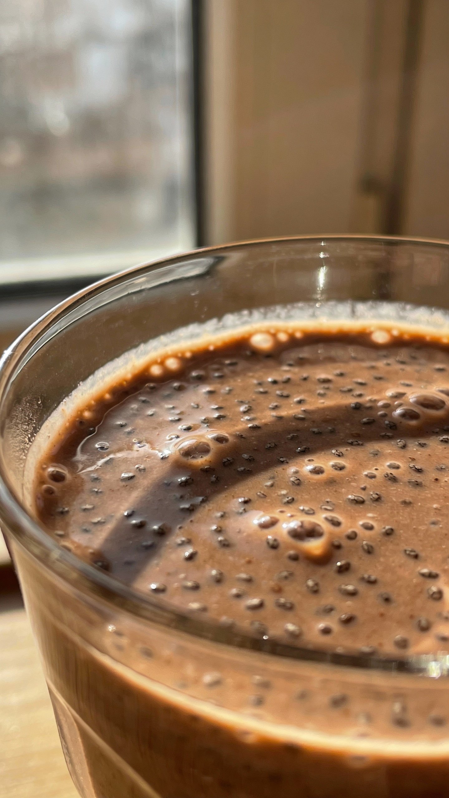 closeup chocolate chia smoothie in clear glass, soft window light