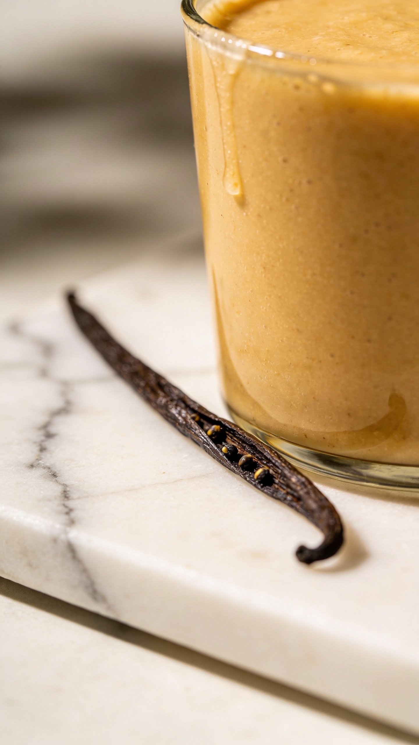 vanilla bean pod on marble beside smoothie rim, shallow focus