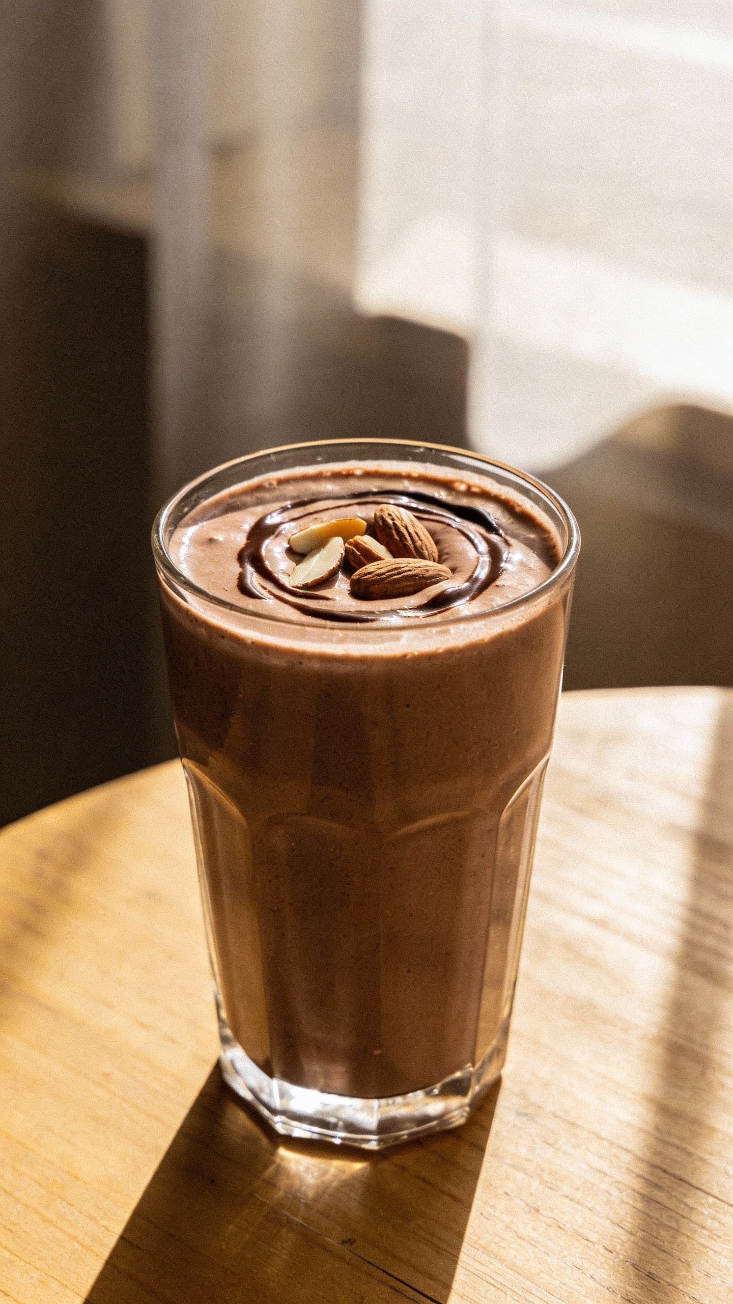 Tall chocolate almond smoothie in clear glass, soft window light