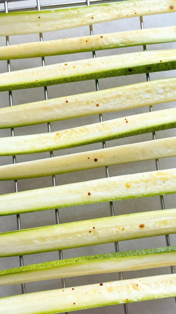 salted zucchini ribbons draining on wire rack, overhead closeup