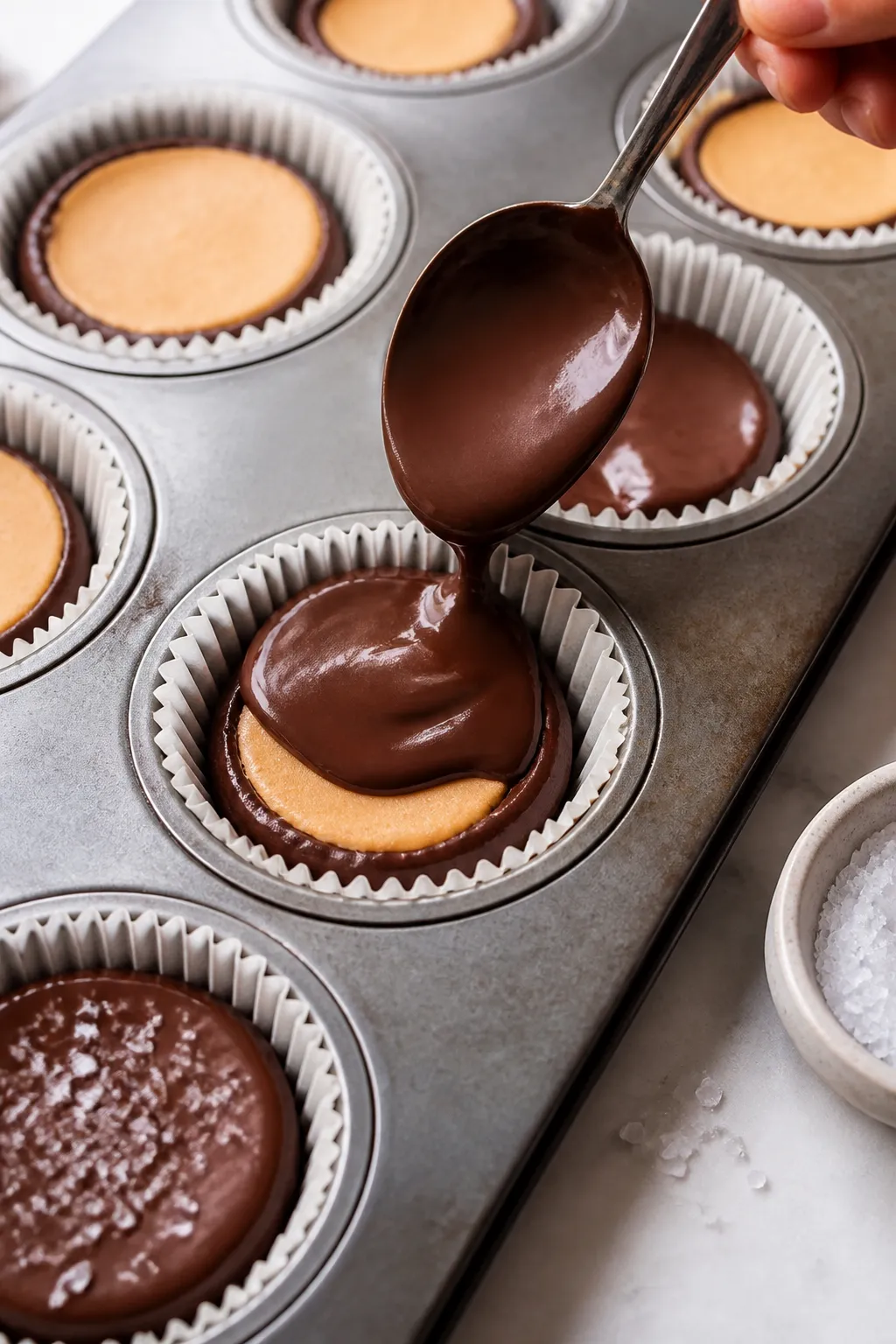 Close-up, process-focused detail of the layering step: a lined muffin tin partially filled, showing 