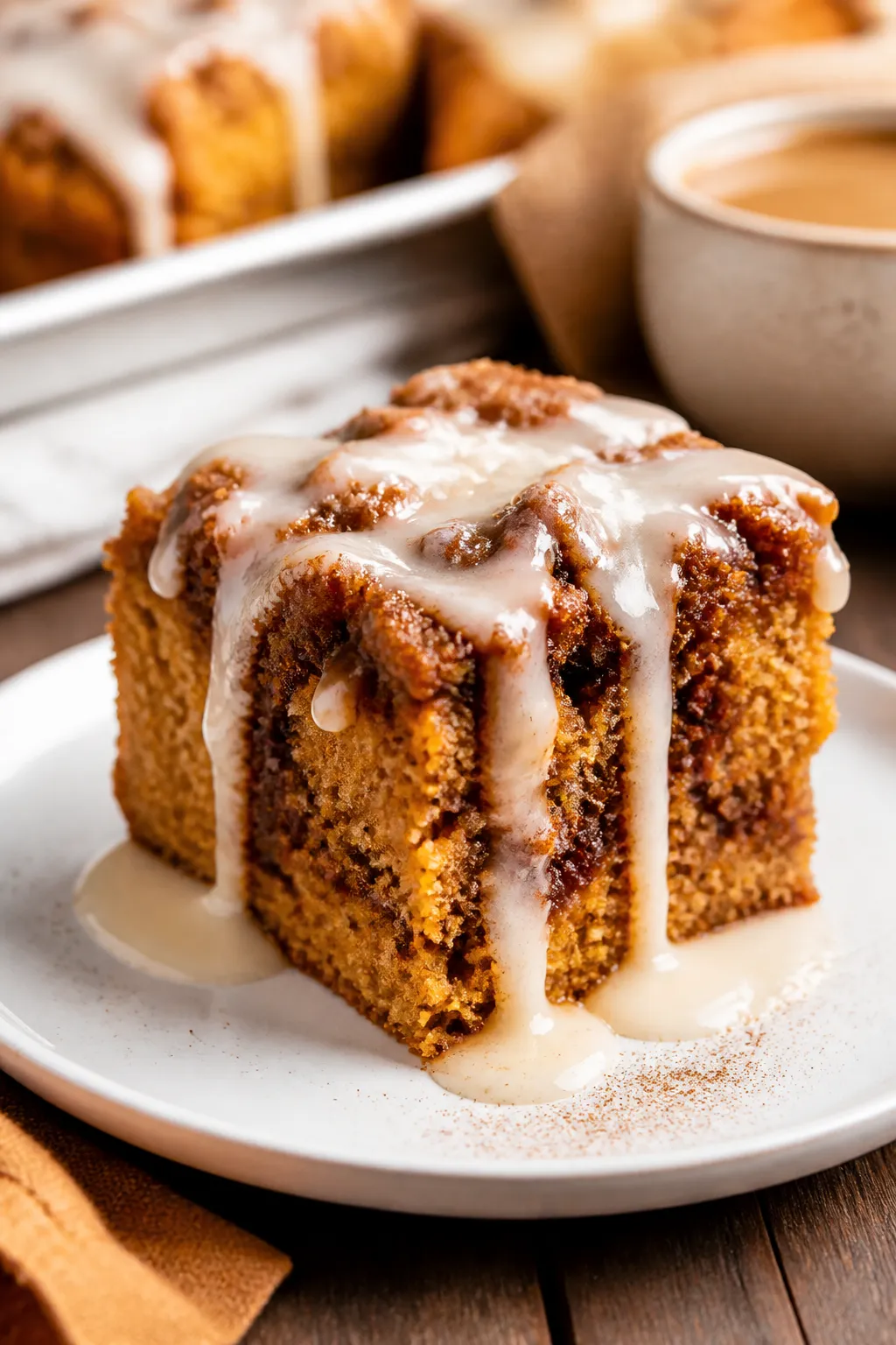 Close-up, three-quarter angle of a warmly sliced square of the pumpkin cinnamon roll cake on a matte