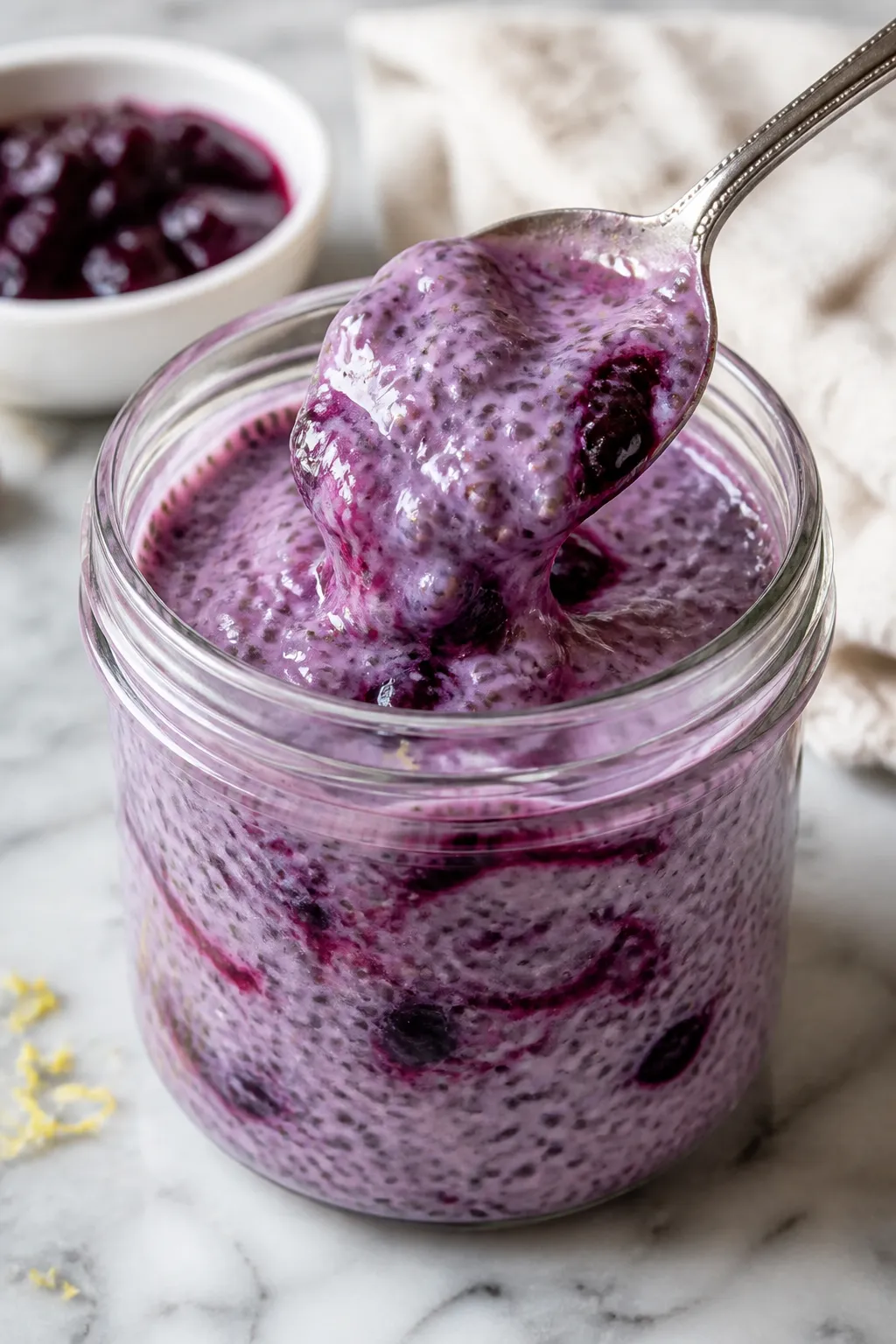 Cooking process close-up: A glass jar on a marble counter mid-prep with thickening blueberry chia pu
