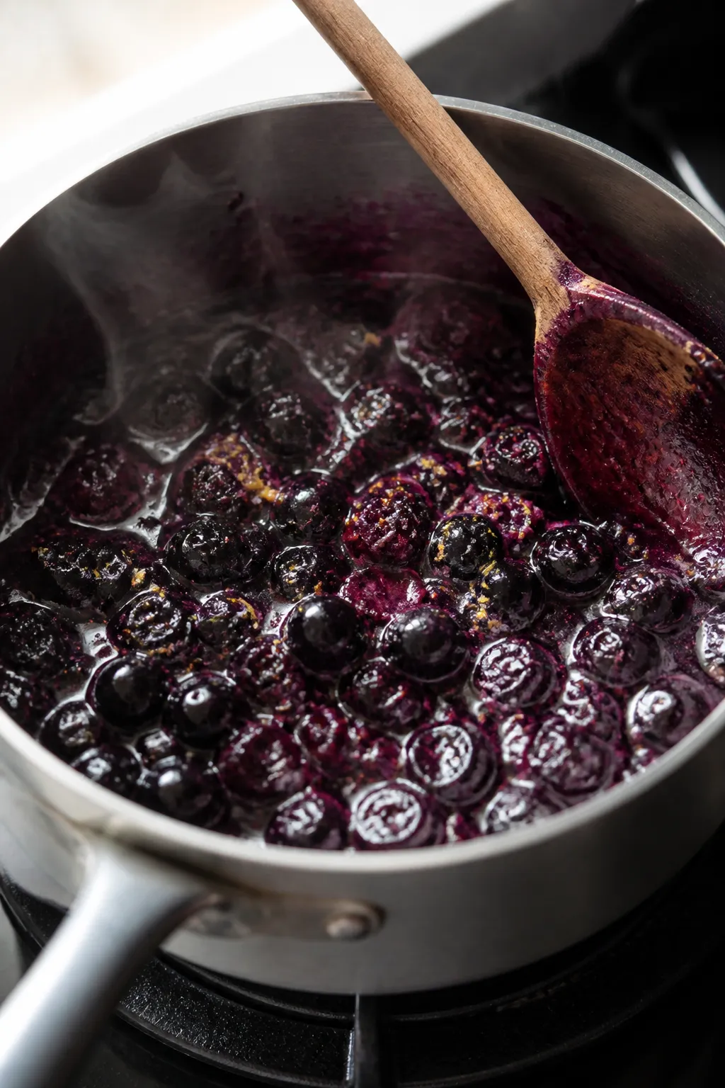 Cooking process close-up: Small saucepan of blueberry compote mid-simmer with several berries just b