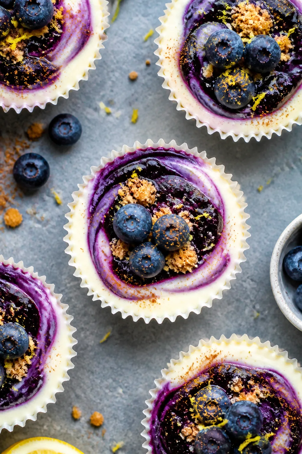 Final dish overhead: High Protein Blueberry Cheesecake Cups set in white paper liners on a cool gray
