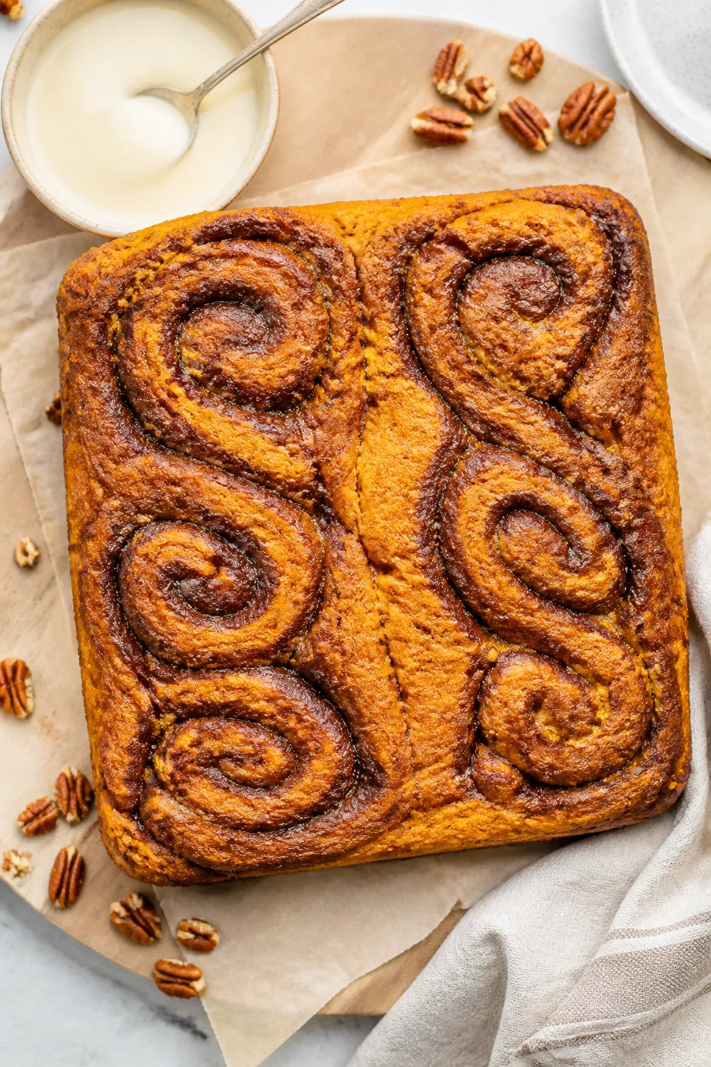 Overhead shot of a just-baked Low Carb Pumpkin Cinnamon Roll Cake lifted from an 8x8 pan on parchmen