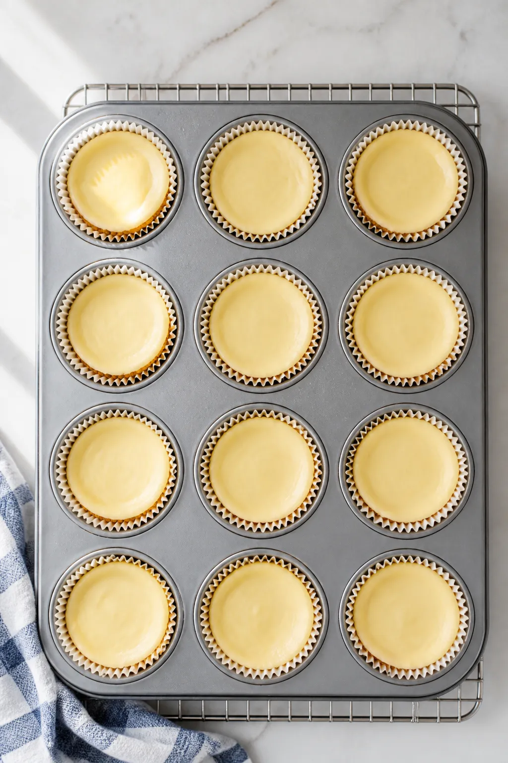 Overhead shot of freshly baked Greek Yogurt Protein Cheesecake Cups cooling in a 12-cup muffin tin,