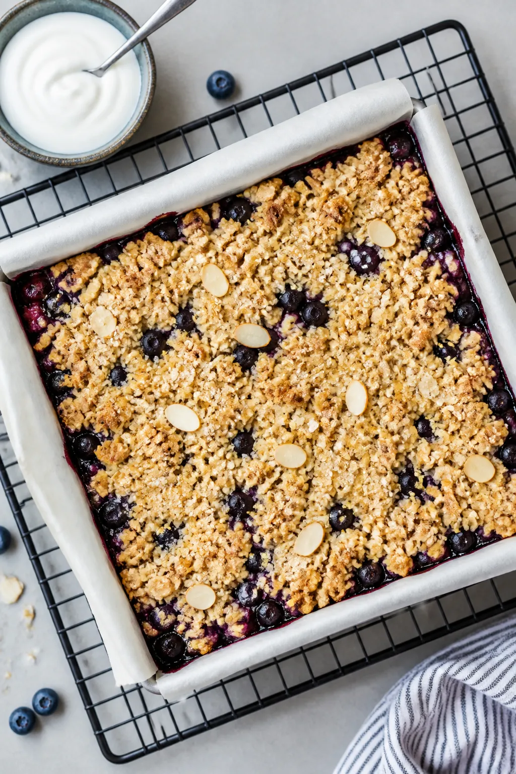 Overhead shot of freshly baked High Protein Blueberry Crumble Bars cooling in an 8-inch parchment-li