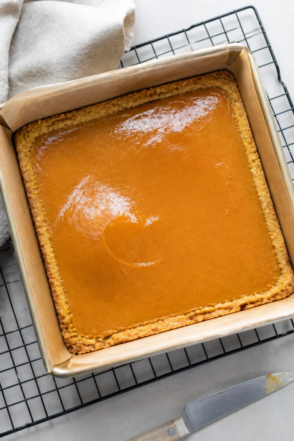 Overhead shot of freshly baked low carb pumpkin pie bars cooling in a parchment-lined 9x9 pan right 