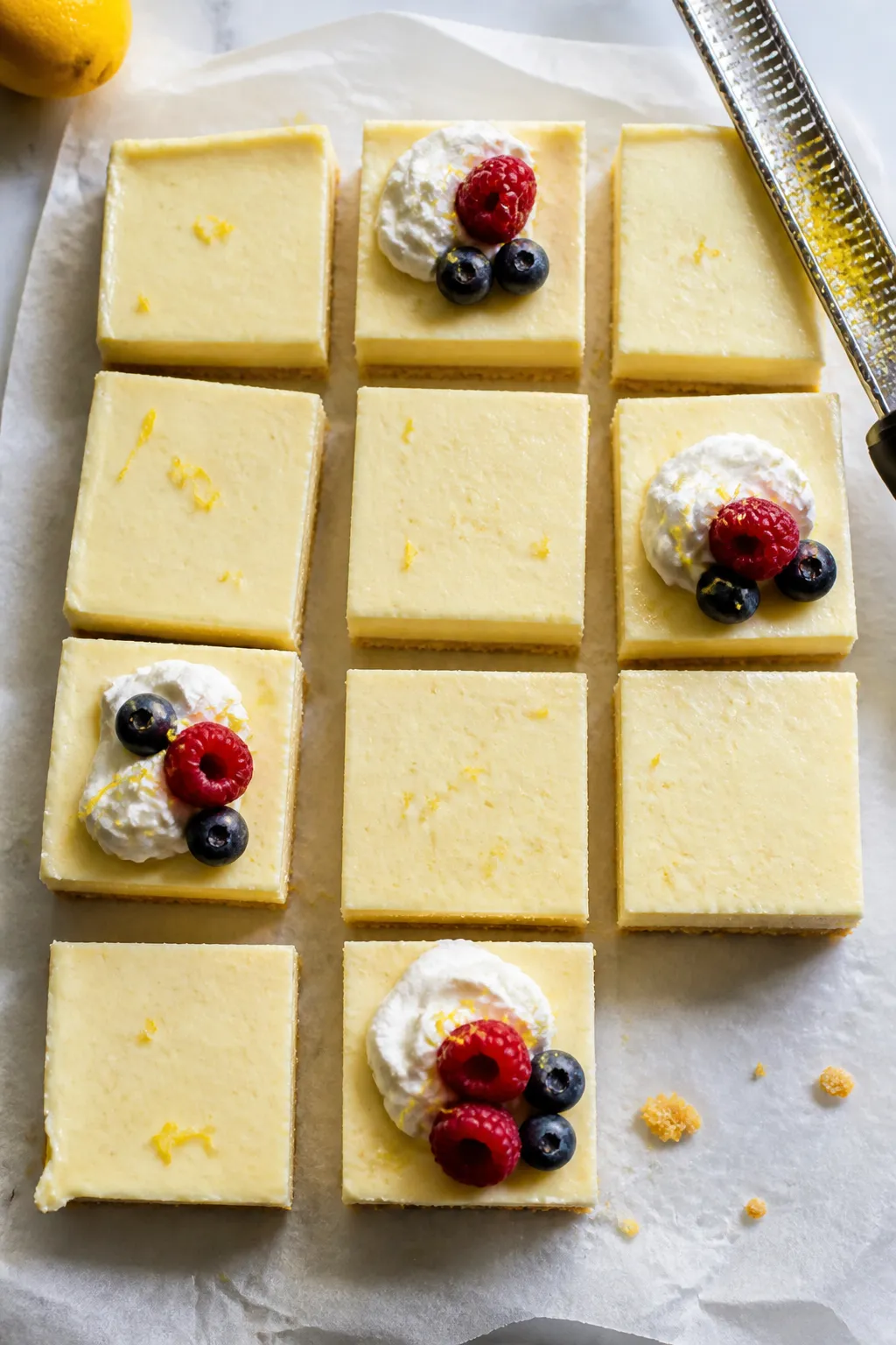 Overhead shot of freshly sliced Low Carb Lemon Cheesecake Bars on parchment lifted from an 8x8 pan,